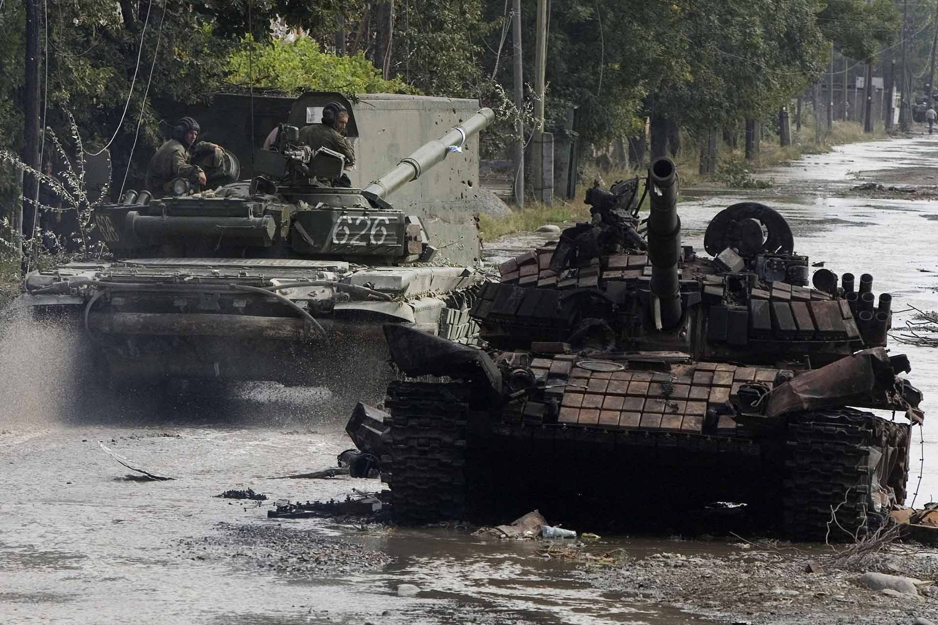 Russian soldiers passing by a destroyed Georgian tank